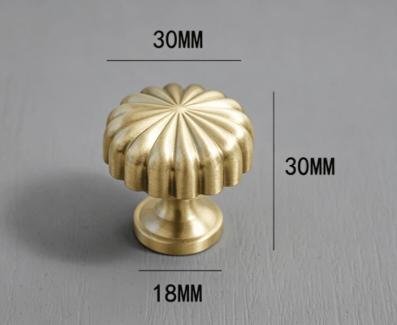 May include: A brass-colored metal cabinet knob with a fluted, circular top and a tapered base. The knob features a brushed finish. Text on the image indicates a diameter of 30mm, a total height of 30mm, and a base diameter of 18mm.