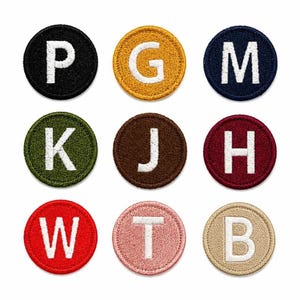 以下が含まれることがあります： 白い大文字が一つずつ刺繍された9枚の円形ワッペンセット。ワッペンは黒、黄色、ネイビーブルー、オリーブグリーン、茶色、マルーン、赤、ライトピンク、ベージュなど、さまざまな色で構成されています。