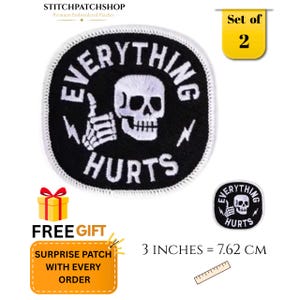 May include: A set of two circular embroidered patches featuring a white skull giving a thumbs up on a black background. The text EVERYTHING HURTS is embroidered in white. A ruler shows the patch measures 3 inches in diameter.