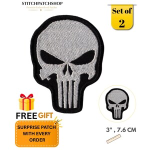 May include: A set of two embroidered patches featuring a stylized silver skull design with black eye sockets and a black border. The patches measure 3 inches in height, as indicated by the visible ruler graphic included in the product display.