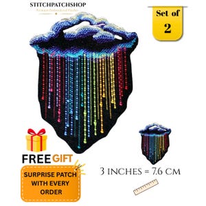 Puede incluir: Un conjunto de dos parches bordados que muestran una nube azul oscuro y morada con gotas de lluvia en colores arcoíris sobre un fondo negro. El texto dice Set of 2 y 3 INCHES = 7.6 CM, junto a una regla y un icono de caja de regalo.