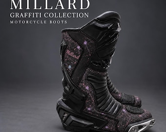 May include: Black motorcycle boots from the Millard Graffiti Collection featuring a dark speckled pattern with pink and blue accents, black protective panels, ribbed ankle sections, and a silver-toned metallic toe slider detail.
