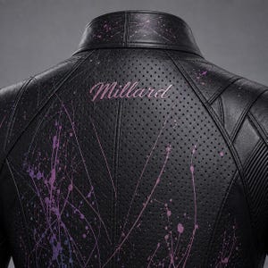 May include: A black perforated leather jacket featuring a high collar and structured paneling. The back displays the word Millard embroidered in pink script, accented by a vibrant purple and pink paint splatter design across the surface.
