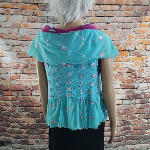 Peut inclure: Un haut turquoise sans manches avec un motif floral rose et un ourlet à volants. Le haut a un col à motif rose et blanc.