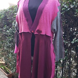May include: A long, open-front cardigan with a pink, gray, and burgundy color scheme. The cardigan has a button closure and a heart-shaped detail on the front.