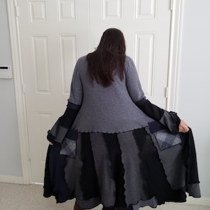 Könnte beinhalten: Ein langer, grauer Strickcardigan mit einem mehrlagigen Patchworkrock in Grautönen und Schwarz. Der Rock hat einen gewellten Saum und eine karierte Tasche.