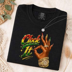 Puede incluir: Una camiseta negra con el texto Clock It en degradado rojo, amarillo y verde. Debajo del texto hay un gráfico de una mano morena haciendo un gesto de ok, adornada con una pulsera de cadena dorada, un reloj dorado y uñas largas doradas.