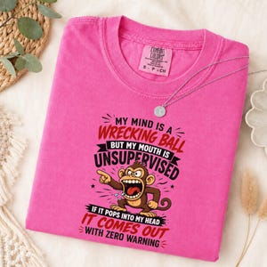 May include: A bright pink short-sleeved t-shirt featuring a graphic of a brown monkey with an open mouth. The text reads: My mind is a wrecking ball but my mouth is unsupervised. If it pops into my head it comes out with zero warning.
