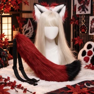 Può includere: Un set di orecchie da animale in pelliccia sintetica e una lunga coda in peluche. Le orecchie sono bianche con punte nere e accenti di pelliccia rossa. La coda è rosso scuro con la punta nera e cinghie in nylon regolabili con fibbie.