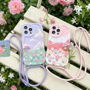 Op de afbeelding: Twee telefoonhoesjes met crossbody koorden. Het linker hoesje is lavendelkleurig met een maan, wolken en tulpen. Het rechter hoesje is roze met een landschap van wolken en kleurrijke bloemen. Beide hebben een camera-uitsparing en glanzende afwerking.