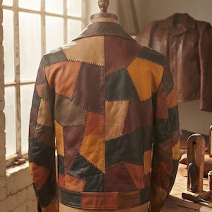 Op de afbeelding: Een patchwork leren jas met een veelkleurig ontwerp in tinten bruin, beige, zwart en oranje. De jas is opgebouwd uit diverse geometrische leren stukken die met zichtbare stiksels aan elkaar zijn gezet, gepresenteerd op een paspop.