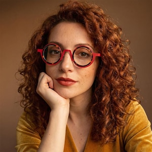 May include: Round eyeglasses featuring a vibrant red frame with a tortoiseshell inner rim pattern. The glasses have a distinct bridge design and clear lenses, providing a bold look that highlights the circular shape of the frames against the face.