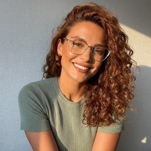 May include: A sage green ribbed short-sleeve top paired with clear-framed glasses and brown tortoiseshell hoop earrings. The garment features a crew neckline and a fitted silhouette, showcasing a textured knit fabric with vertical ribbed detailing.