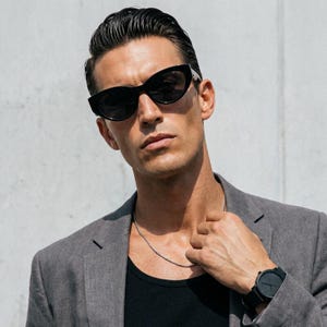 Può includere: Occhiali da sole neri a forma di gatto con lenti scure, un blazer grigio, una maglietta nera, una sottile collana a catena argentata e un orologio da polso nero con quadrante rotondo e cinturino in silicone indossati insieme.