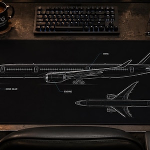 Pode incluir: Um tapete de secretária preto com um desenho técnico de linhas brancas de um avião comercial em perfis lateral e superior. O design inclui etiquetas para o cockpit, trem de aterragem, motor, asa e estabilizador em estilo esquemático.