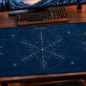 May include: A rectangular dark blue desk mat featuring white technical blueprint-style snowflake illustrations. The design includes labeled circles with diameters of 8.00 inches and 16.00 inches, accented by corner illustrations of pine branches with red berries.