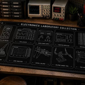 May include: A rectangular black desk mat featuring white line art illustrations of electronics laboratory equipment. The text reads Electronics Laboratory Collection, with labels for a digital multimeter, oscilloscope, power supply, and other tools.