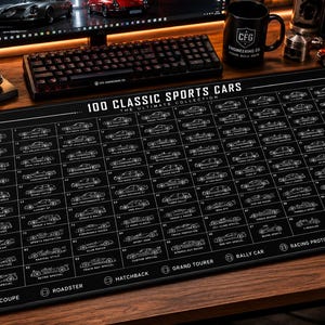 May include: A black rectangular desk mat featuring a white grid of 100 classic sports cars, each labeled with a number and name. The top text reads 100 CLASSIC SPORTS CARS THE ULTIMATE COLLECTION, with various car categories listed along the bottom edge.