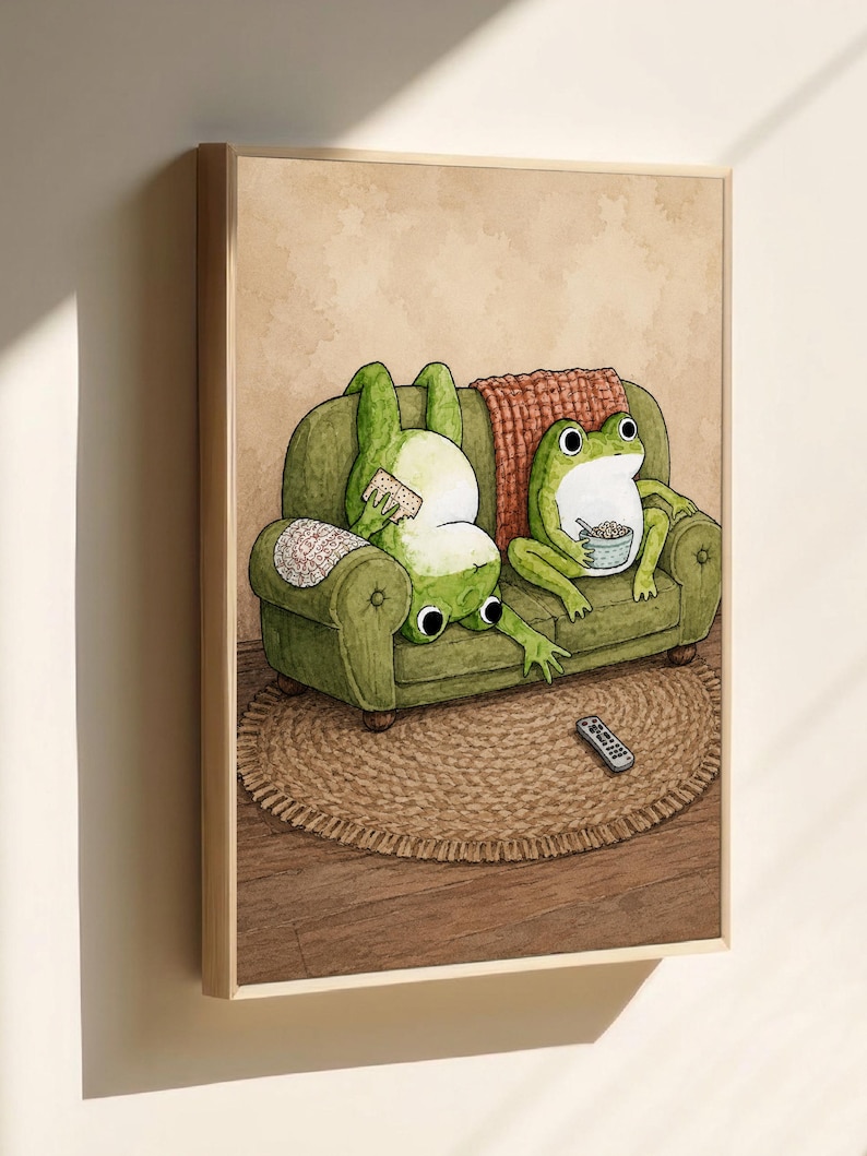 Puede incluir: Una l&aacute;mina art&iacute;stica enmarcada que muestra dos ranas verdes en un sof&aacute; verde. Una rana est&aacute; boca abajo sosteniendo una galleta, mientras que la otra est&aacute; sentada sosteniendo un taz&oacute;n de cereales. Un mando a distancia descansa sobre una alfombra.