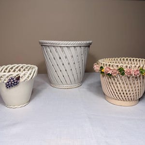 May include: Three ceramic baskets with woven lattice designs. The left basket is white with a purple grape accent. The centre basket is white with a rope-style rim. The right basket is cream-coloured and features a decorative ring of pink roses.