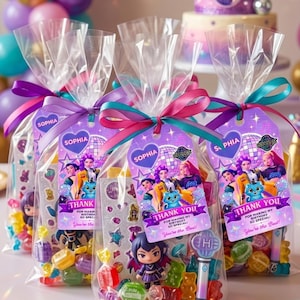 Può includere: Tre sacchetti regalo in plastica trasparente riempiti con caramelle colorate, una piccola statuetta e un foglio di adesivi. Ogni sacchetto è legato con un nastro viola e verde acqua e presenta un'etichetta con il nome Sophia e Thank You.