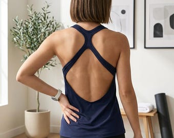May include: A dark navy blue vest top featuring a racerback design with a large, open back cutout. The garment is sleeveless with a rounded neckline and a fitted silhouette, constructed from a smooth, solid-coloured fabric suitable for athletic activity.
