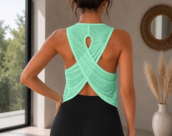 May include: A light green sleeveless tank top featuring a textured, semi-sheer fabric with a distinctive crisscross back design and a small teardrop-shaped cutout at the upper back, paired with solid black leggings that sit at the waist.