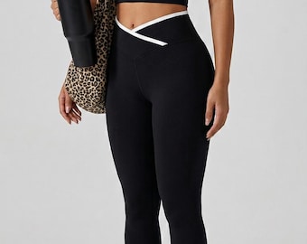 May include: A black athletic crop top with white trim and matching black leggings featuring a V-shaped crossover waistband with white trim. The outfit is paired with white crew socks, white athletic trainers, and a leopard print tote bag.