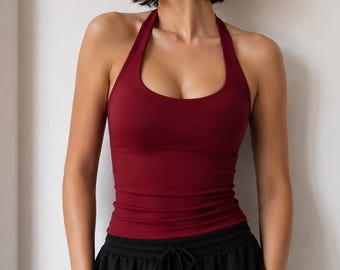 May include: A deep burgundy halter-neck tank top with a scoop neckline and a fitted silhouette, paired with black athletic pants featuring an elastic waistband and a drawstring closure. The top is sleeveless and made of a smooth, solid-colored fabric.