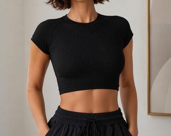 May include: A black ribbed short-sleeve crop top with a crew neckline paired with black drawstring sweatpants. The top features a fitted silhouette with textured vertical ribbing, while the pants have an elastic waistband and side pockets.