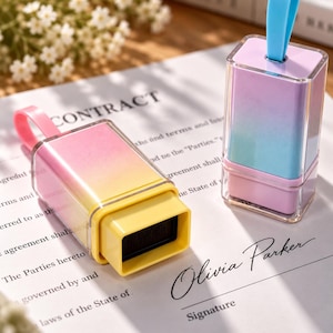 May include: Two rectangular identity theft protection stamps with clear plastic covers. One stamp features a pink-to-yellow gradient with a pink pull tab, while the other has a purple-to-blue gradient with a blue pull tab and a black ink pad.