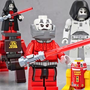 May include: A collection of four plastic building block figures including a character in a red suit with a red lightsaber, a character in a black cloak with a red lightsaber, a white armored character, and a small red and yellow droid figure.