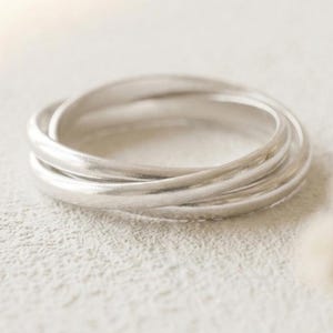 May include: A silver-colored ring composed of three interlocking bands. The metal has a smooth, polished finish with a reflective surface. The three circular bands are connected and overlap each other to form a single cohesive jewelry piece.