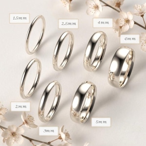 Puede incluir: Una colección de siete anillos de metal plateado pulido dispuestos en grupo, cada uno etiquetado con su ancho específico, incluyendo 1,5 mm, 2 mm, 2,5 mm, 3 mm, 4 mm, 5 mm y 6 mm. Los anillos presentan un diseño de banda lisa y redondeada.