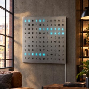 Könnte beinhalten: Eine quadratische Wanduhr mit metallischem Finish und einem Raster aus schwarzen Buchstaben. Die Uhr zeigt die Zeit mit leuchtend cyanfarbenem Text an, der ES BIST VIERTEL NACH SIEBEN lautet, was Viertel nach sieben bedeutet.