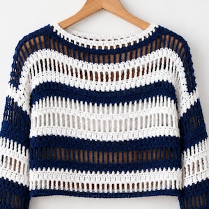 May include: A long-sleeve crochet sweater featuring horizontal stripes in navy blue and white. The garment has a wide boat neckline and an open-knit construction with alternating solid and vertical bar patterns throughout the body and sleeves.