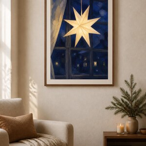 May include: A framed wall art print depicting a glowing, multi-pointed paper star hanging in a window at night. The scene shows a dark blue exterior view through the window panes, with a light-colored curtain draped to the side of the frame.