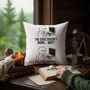 May include: A white square throw pillow featuring a black line art comic strip. The top panel shows a person at a computer with the text THE CODE DOESN'T WORK... WHY? The bottom panel shows the same person with the text THE CODE WORKS... WHY?