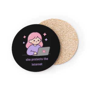 May include: A round black coaster featuring a cartoon illustration of a person with pink hair using a laptop with a red lock icon on the lid. The text "she protects the internet" is printed below in light purple. A second cork coaster is visible behind.