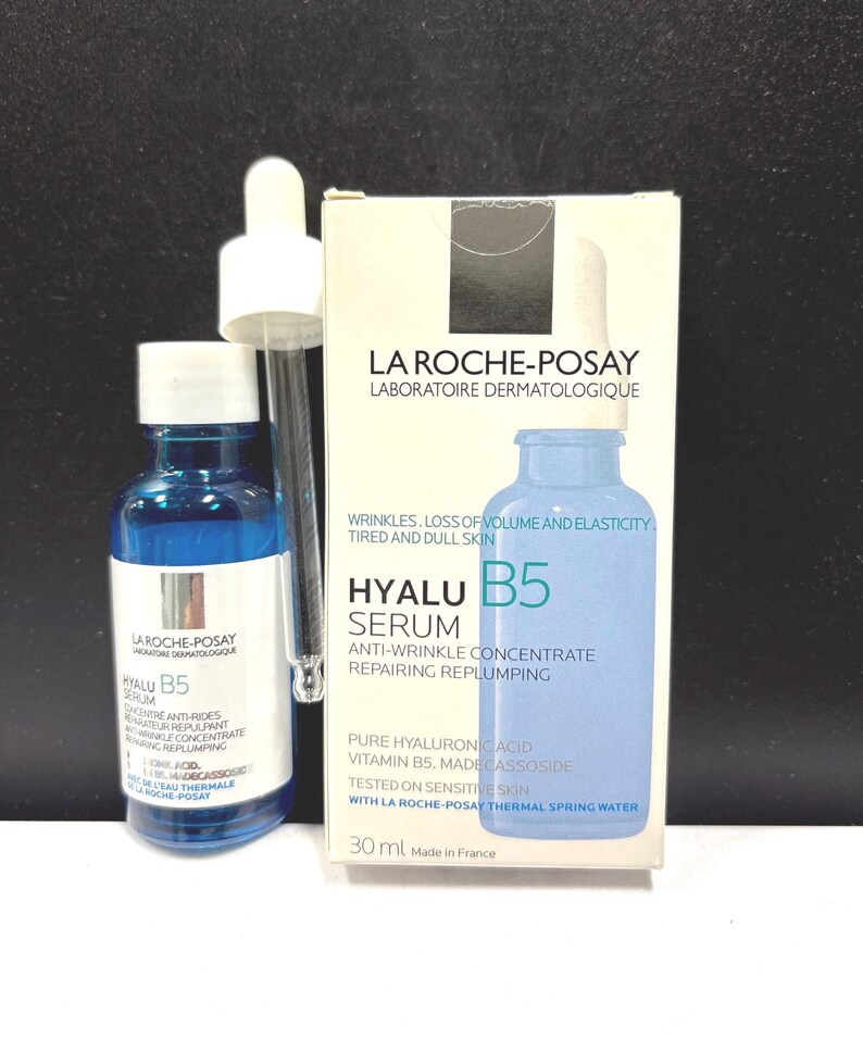 May include: A blue glass bottle of La Roche-Posay Hyalu B5 serum with a white dropper cap, accompanied by its white cardboard box. The packaging features the text: La Roche-Posay, Hyalu B5 Serum, Anti-Wrinkle Concentrate, Repairing Replumping, 30 ml.
