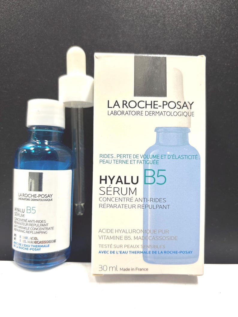 May include: A blue glass bottle of La Roche-Posay Hyalu B5 serum with a white dropper cap, accompanied by its white cardboard packaging box. The box features the product name, ingredients like hyaluronic acid and vitamin B5, and 30 ml volume.