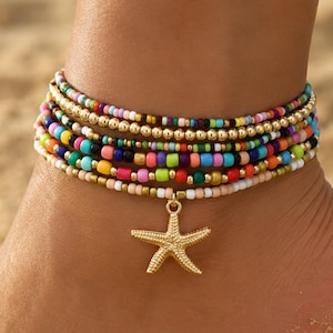 May include: A multi-layered anklet featuring several strands of small, colorful glass beads in shades of blue, pink, yellow, green, and red, interspersed with metallic gold beads and a central gold-toned starfish charm dangling from the bottom strand.