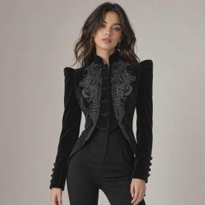 Peut inclure: Une veste en velours noir dotée de manches longues avec poignets boutonnés, d'un col montant et de broderies noires complexes sur les panneaux avant. La veste présente des épaules structurées et une fermeture à boutons, portée avec un pantalon noir.