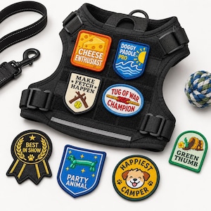 May include: A black tactical dog harness with adjustable straps and a reflective strip, featuring several embroidered patches including Cheese Enthusiast, Doggy Paddle Pro, Make Fetch Happen, Tug of War Champion, Best in Show, Party Animal, Happiest Camper, and Green Thumb.