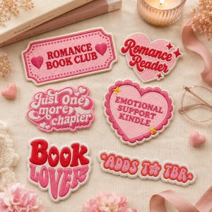 May include: Six embroidered patches in shades of pink and red. The patches feature text including Romance Book Club, Romance Reader, Just One More Chapter, Emotional Support Kindle, Book Lover, and Adds To TBR, decorated with hearts and stars.