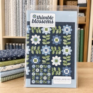 May include: A quilt pattern booklet titled Thimble Blossoms by Camille Roskelley, featuring a dark blue background with a repeating floral design in shades of light blue, white, and green. The cover displays the text Edelweiss and number 278.