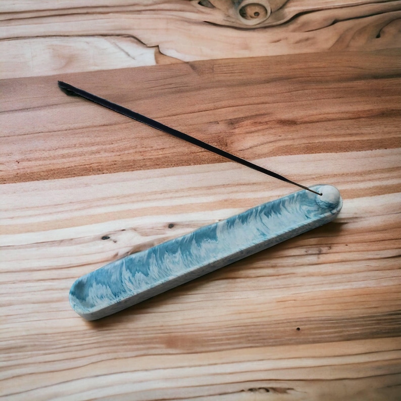 Blue marble Jesmonite incense holder with incense stick resting at an angle, overhead view on a wooden surface, Croft & Cleo