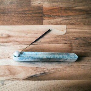 Blue marble Jesmonite incense holder with lit incense stick, angled view showing the marbled surface and wood backdrop, Croft & Cleo