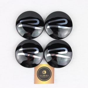 Puede incluir: Cuatro tapacubos circulares negros, cada uno con un logotipo R plateado estilizado. Debajo de los tapacubos hay una pequeña tarjeta cuadrada con un logotipo circular dorado y el texto ALL CAR DITZ, You know you need it, en negro y dorado.