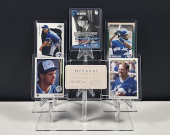 May include: A clear acrylic tiered display stand holding five baseball trading cards and a rectangular white card with the text HIYASAT EXHIBITION CURATED WITH PURPOSE HEX-TBJ-002 ONE-OF-ONE. The stand features multiple levels to showcase the cards.